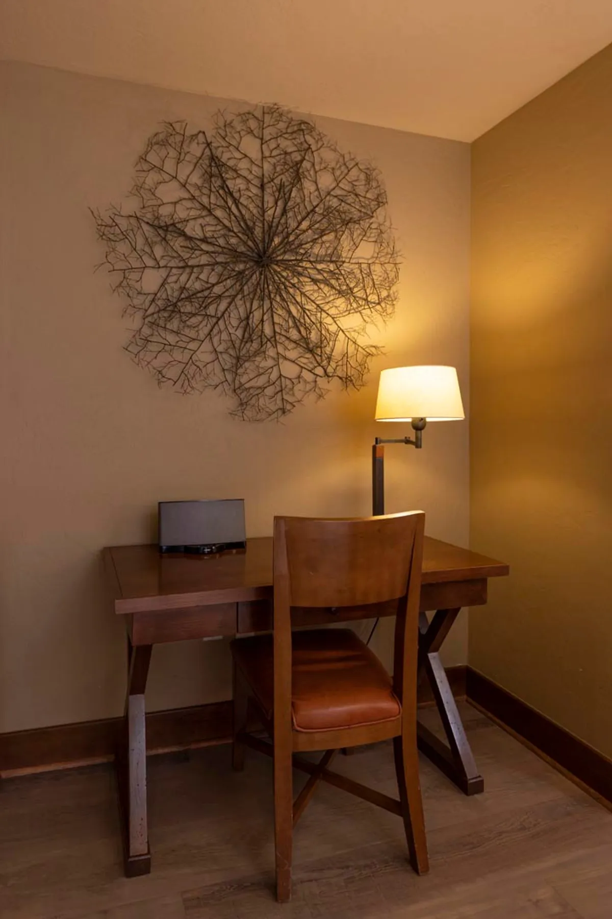 A dedicated workspace with a wooden desk, chair, unique branch wall art, and a desk lamp creates an inviting environment for productivity and inspiration.