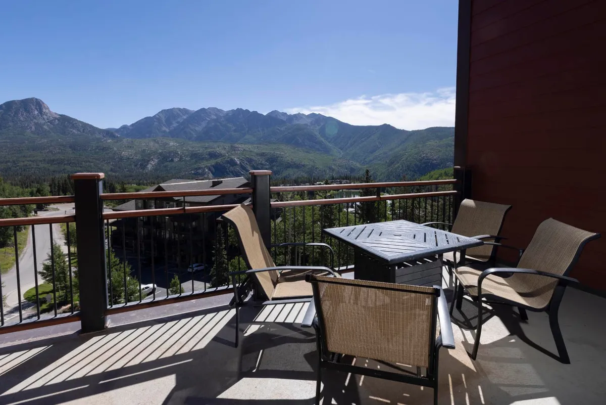 A private balcony outfitted with comfortable seating and a table, overlooking breathtaking mountain vistas. The serene morning light suggests peaceful moments spent sipping coffee or toasting to another day in the mountains, with fresh air and natural beauty all around.