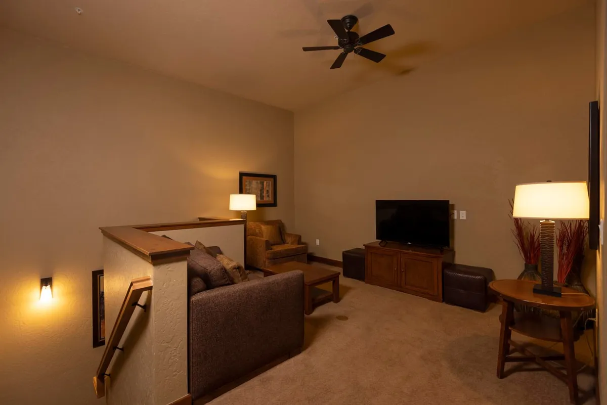 An airy upstairs loft with a comfortable sofa, armchair, TV, table lamps, and a ceiling fan. The relaxed atmosphere makes it a perfect spot for watching movies, reading, or enjoying some solo downtime.