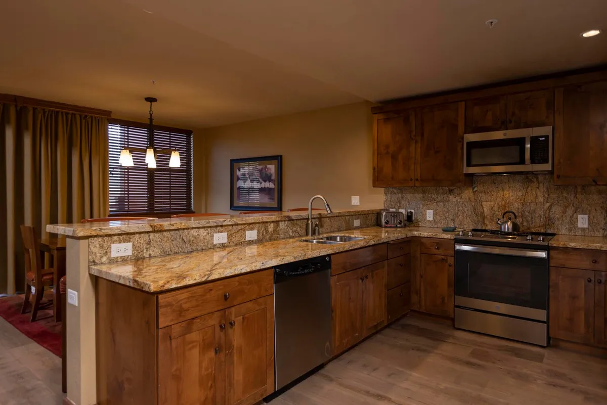 This image features a cozy, functional kitchen with granite countertops, wooden cabinets, and stainless steel appliances. The space is designed for cooking, entertaining, and gathering, suggesting lively meals and social interaction.