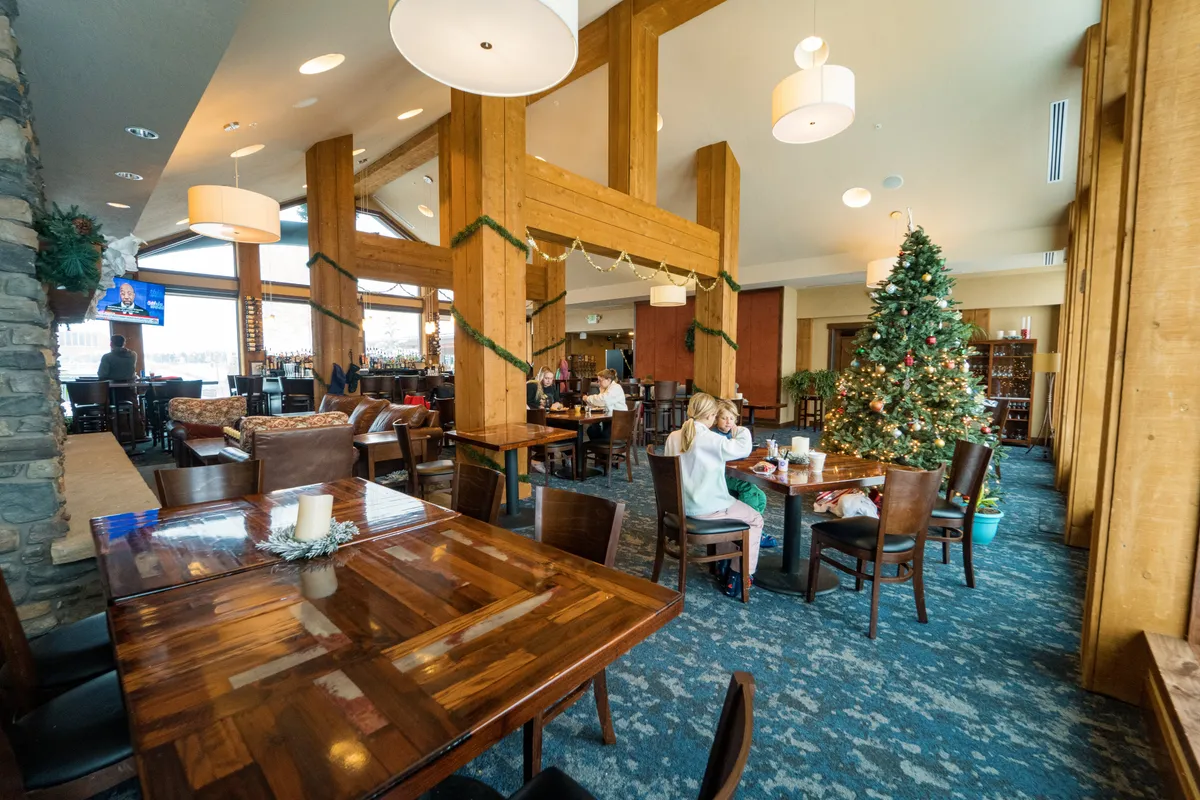 A spacious guest lounge or restaurant area features large wooden beams, festive decorations, a Christmas tree, dining tables, and a bar area. The mood is warm, social, and inviting—ideal for gatherings and celebrations.