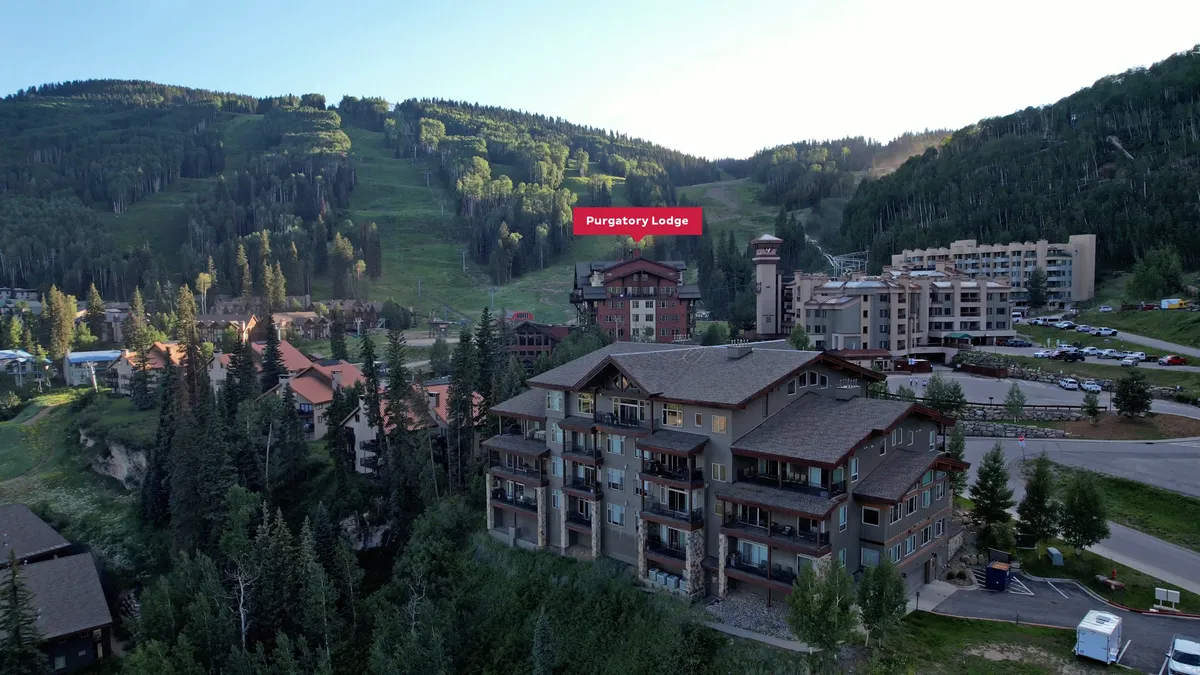 This exterior image showcases Purgatory Lodge with ski slopes, surrounding mountains, and a parking area, all covered in snow. The lodge is prominently set against the backdrop of the mountains, with ski runs clearly visible leading right up to the building.