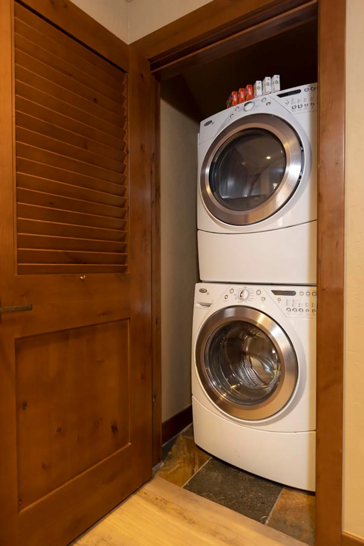 An interior image featuring a practical entry space with a stacked washer and dryer next to a wooden door. The slatted door suggests storage, possibly adjacent to a ski locker or similar facility.